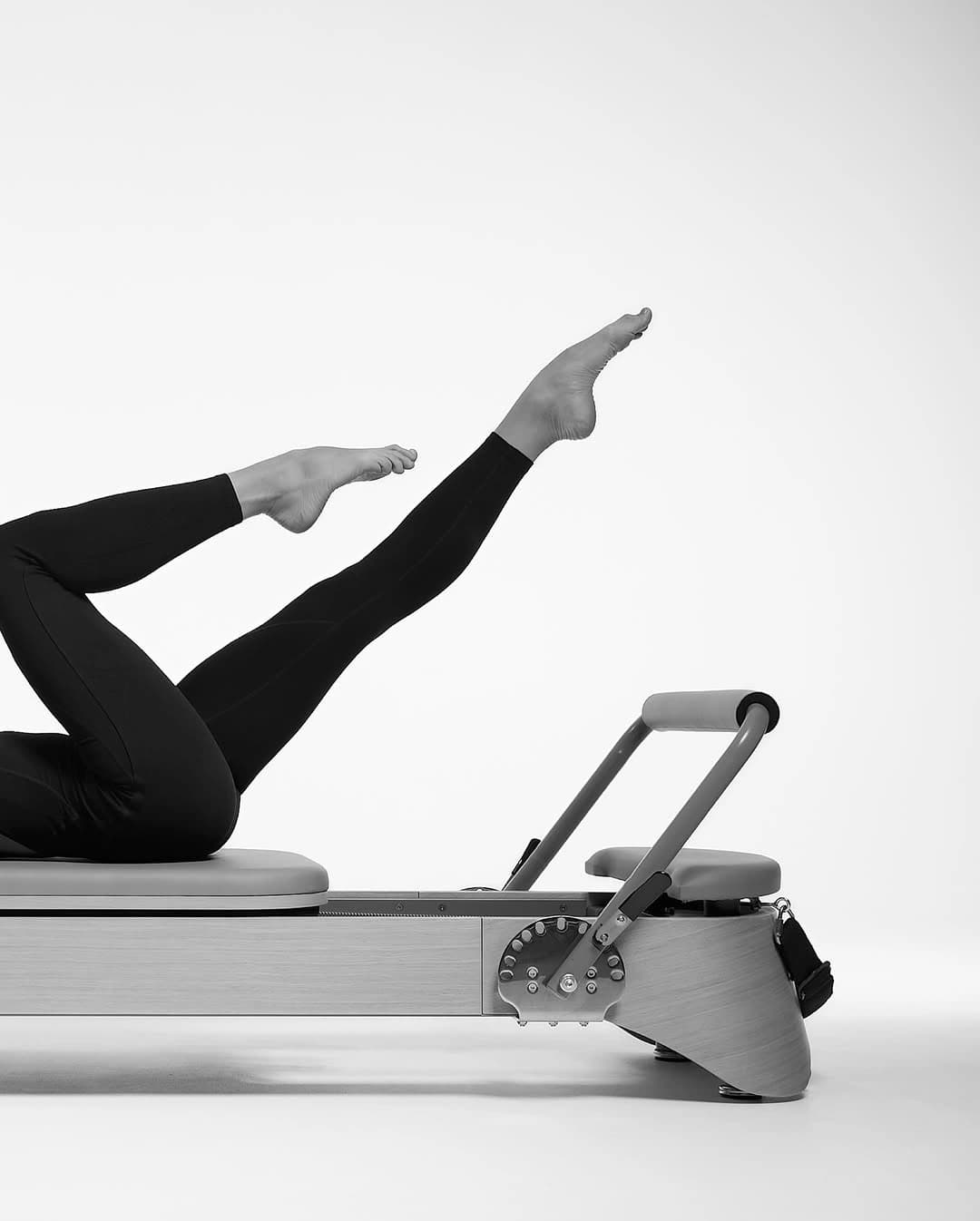 Legs extended on a Pilates reformer, black and white
